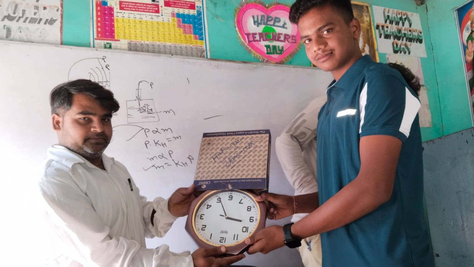 A teacher hands a wall clock to a Class 12 student as a prize in the classroom